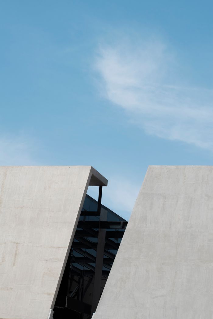 about-us Minimalist concrete building with blue sky and clouds.