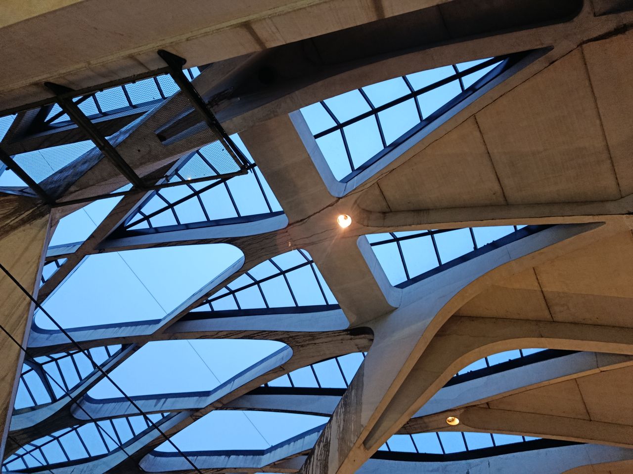 home-hero Abstract view of a modern ceiling design featuring concrete beams and skylights.